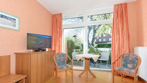 Una habitación con televisión, dos sillas, una mesita y una ventana con cortinas.