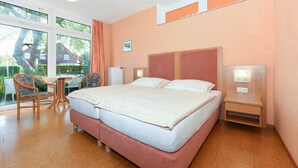 Una cama doble con cabecera de madera, una mesita con sillas y vistas al exterior a través de amplios ventanales.