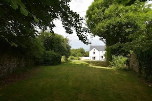 A white house with a well-maintained lawn and dense foliage surrounding it.