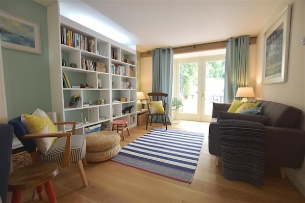 A living room with a bookshelf, a sofa, a chair, a rug, and a window with curtains.