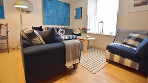 A living room with two sofas, a coffee table, and a lamp. There is a large window providing natural light. - Gwelfor, Newport (Fishguard)