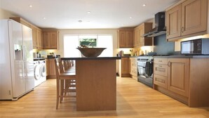 A modern kitchen with wooden cabinets, a central island, and built-in appliances. - Gwelfor, Newport (Fishguard)
