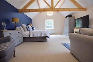 A bedroom with a sloped ceiling, a bed, a dresser, a TV, and a window.