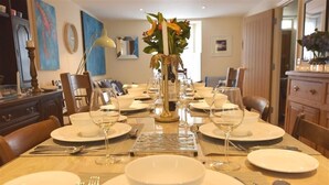 A dining area with a long table set for a meal, surrounded by chairs, with a vase of flowers in the center. - Gwelfor, Newport (Fishguard)
