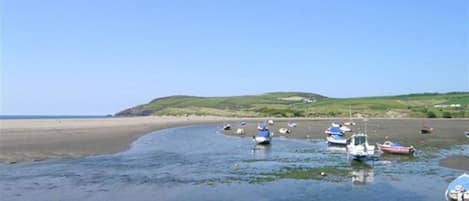 A coastal scene with boats on a sandy beach and calm water.
