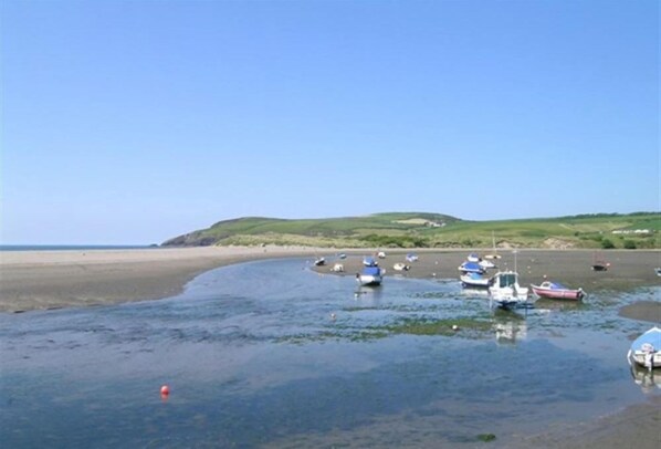 A coastal scene with boats on a sandy beach and calm water.