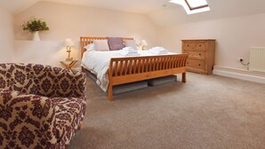 Une chambre avec un lit en bois, une table de chevet, une commode et une chaise. Il y a des fenêtres de toit au plafond.