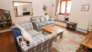 Un salon chaleureux avec un canapé, une table basse et un banc en bois. Il y a une fenêtre avec des rideaux, un radiateur et un miroir au mur.