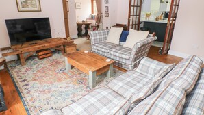 Un salon avec un téléviseur, une table basse en bois, un canapé à motifs écossais et un tapis à motifs.