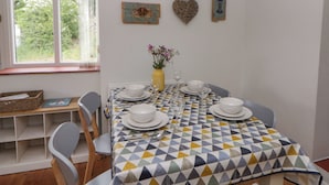 A dining area with a table set for four, chairs, a vase with flowers, and wall decorations including a fish, a crab, a heart, and a bird. - Little Barn Cottage (Newport)