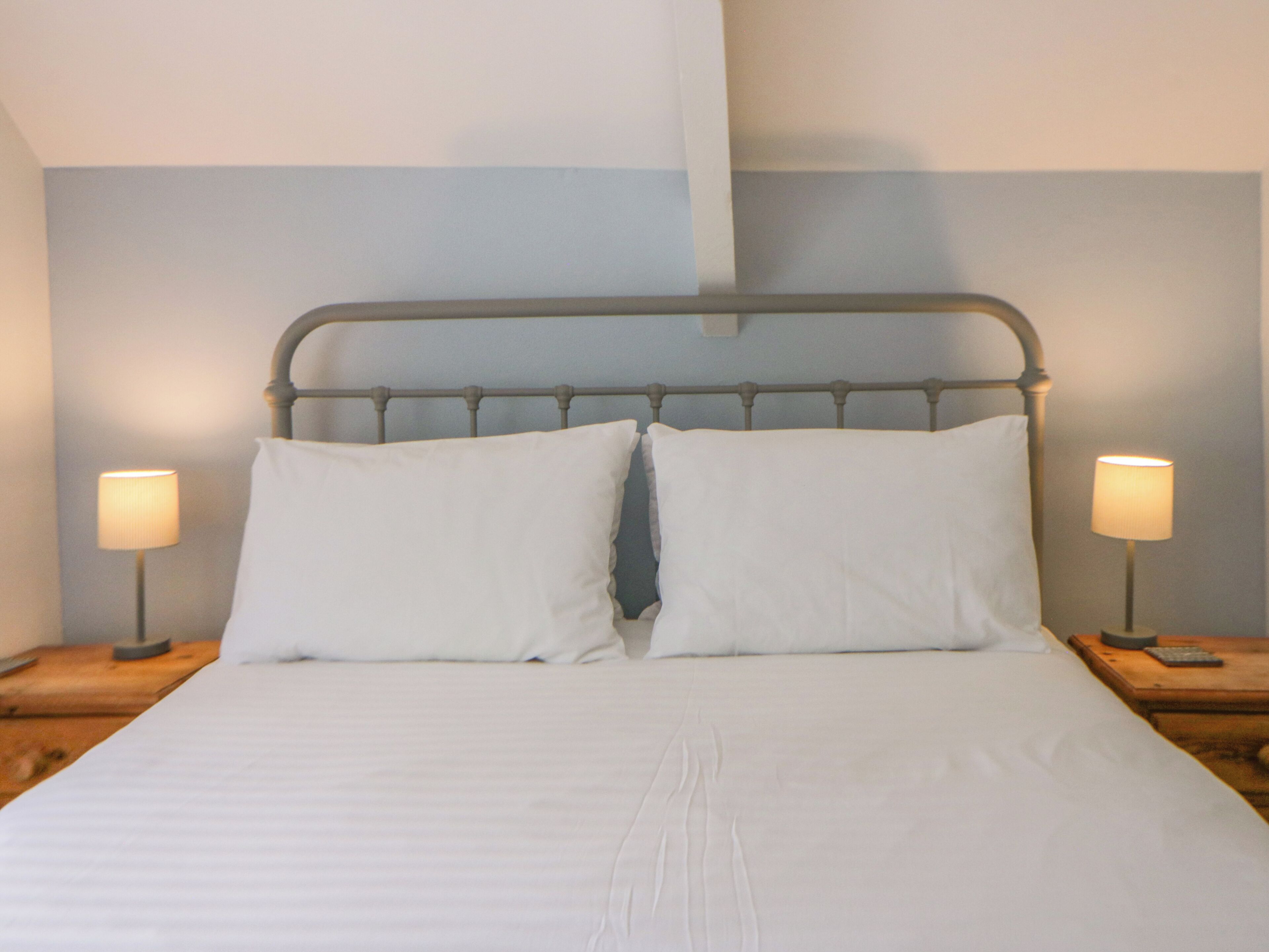 A bed with white linens, a metal headboard, and two bedside lamps on wooden nightstands.