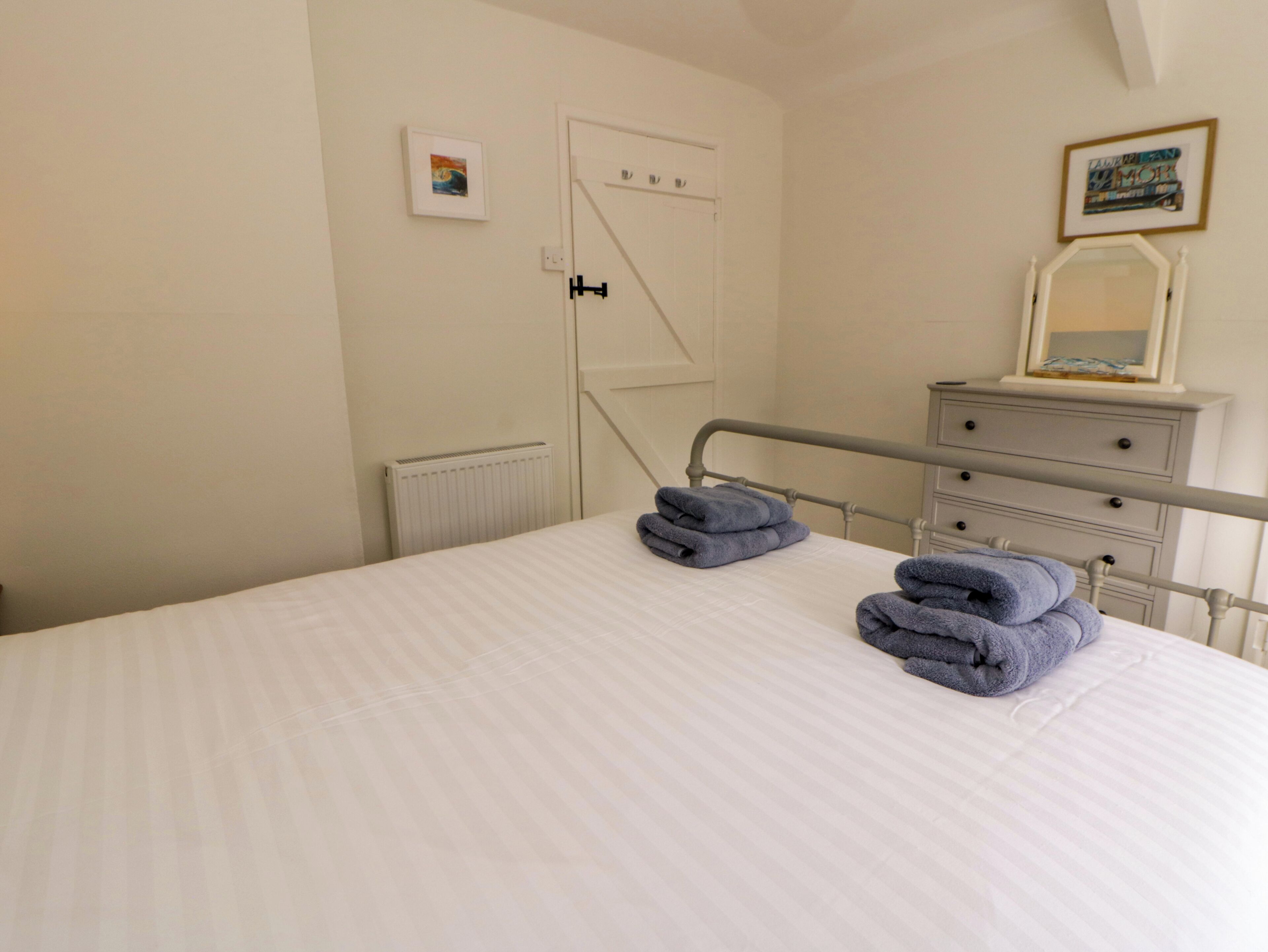 Un dormitorio con cama, radiador, cómoda, espejo y una puerta.