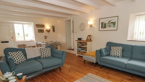 A living room with two sofas, a wooden coffee table, a rug, a dining table with chairs, and a bookshelf. - Little Barn Cottage (Newport)