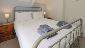 A neatly made bed with pillows, a bedside table with a lamp, and a folded towel on the bed. - Little Barn Cottage (Newport)