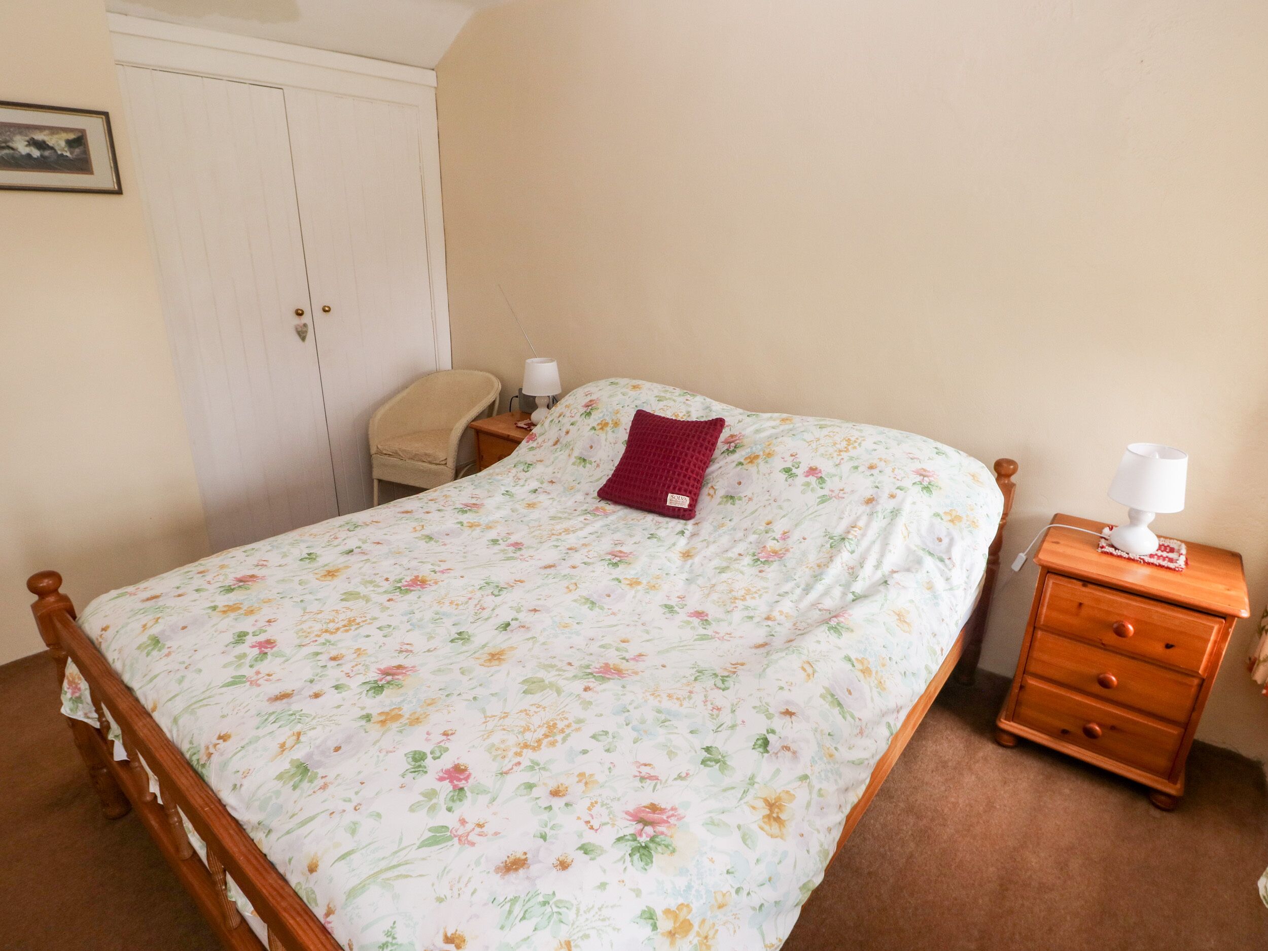 A bedroom with a wooden bed, a nightstand with a lamp, a chair, and a wardrobe.