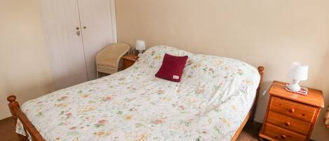 A bedroom with a wooden bed, a nightstand with a lamp, a chair, and a wardrobe.