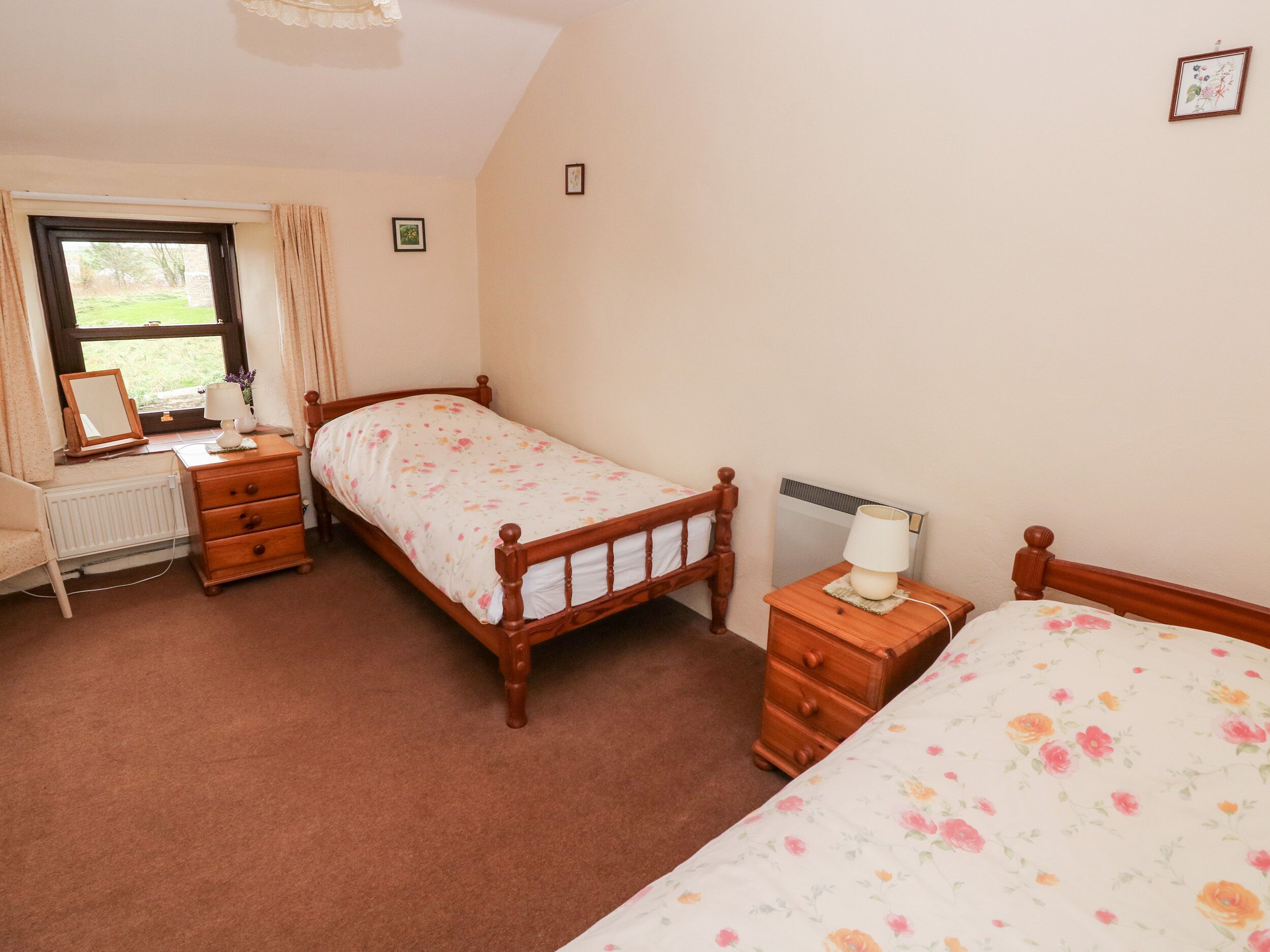 A bedroom with a double bed, a bedside table with a lamp, a dresser, a window with curtains, and a radiator.