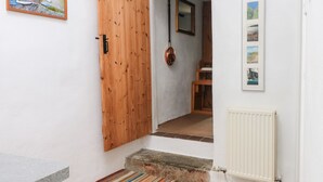 Un pasillo con puerta de madera, un radiador, un tapete a rayas y un cuadro en la pared.