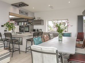 A modern kitchen with a central island, bar stools, and a dining table with chairs. - Hafod Y Mor (Criccieth)