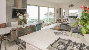Una cocina moderna con estufa a gas, comedor con sillas y un ventanal con vista al mar.