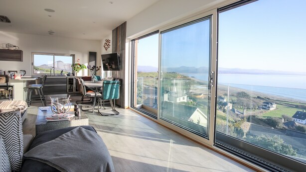 Amplia sala de estar con un gran ventanal corredizo que da a un balcón con vistas panorámicas al mar y las colinas.