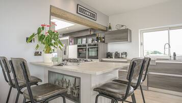 A modern kitchen with a central island, bar stools, a potted plant, and a view of the outdoors.