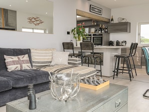 A modern living room with a grey sofa, striped cushions, a chessboard, and a telescope on a coffee table. - Hafod Y Mor (Criccieth)
