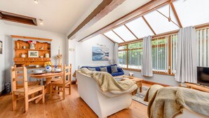 A cozy living room with a sofa, wooden chairs, a dining table, and a kitchen area with wooden shelves. - Covert Farm Cwtch (Kilgetty)
