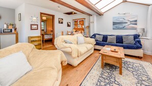 A cozy living room with a high ceiling, wooden beams, a large window, a blue sofa, a beige sofa, and a wooden coffee table. - Covert Farm Cwtch (Kilgetty)