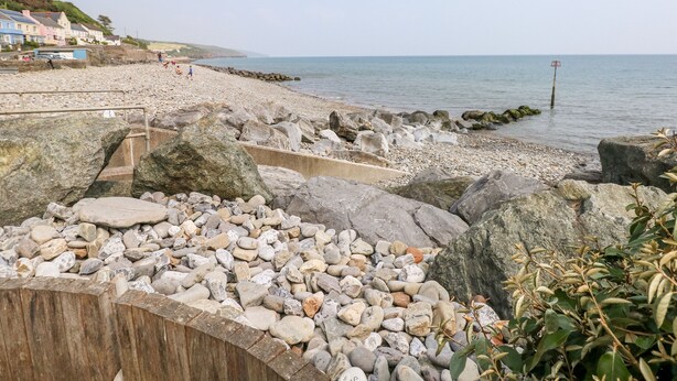 A rocky beach with a wooden walkway leading to a row of houses. - Covert Farm Cwtch (Kilgetty)