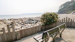 A bench by a rocky beach with a wooden fence and a bush. - Covert Farm Cwtch (Kilgetty)