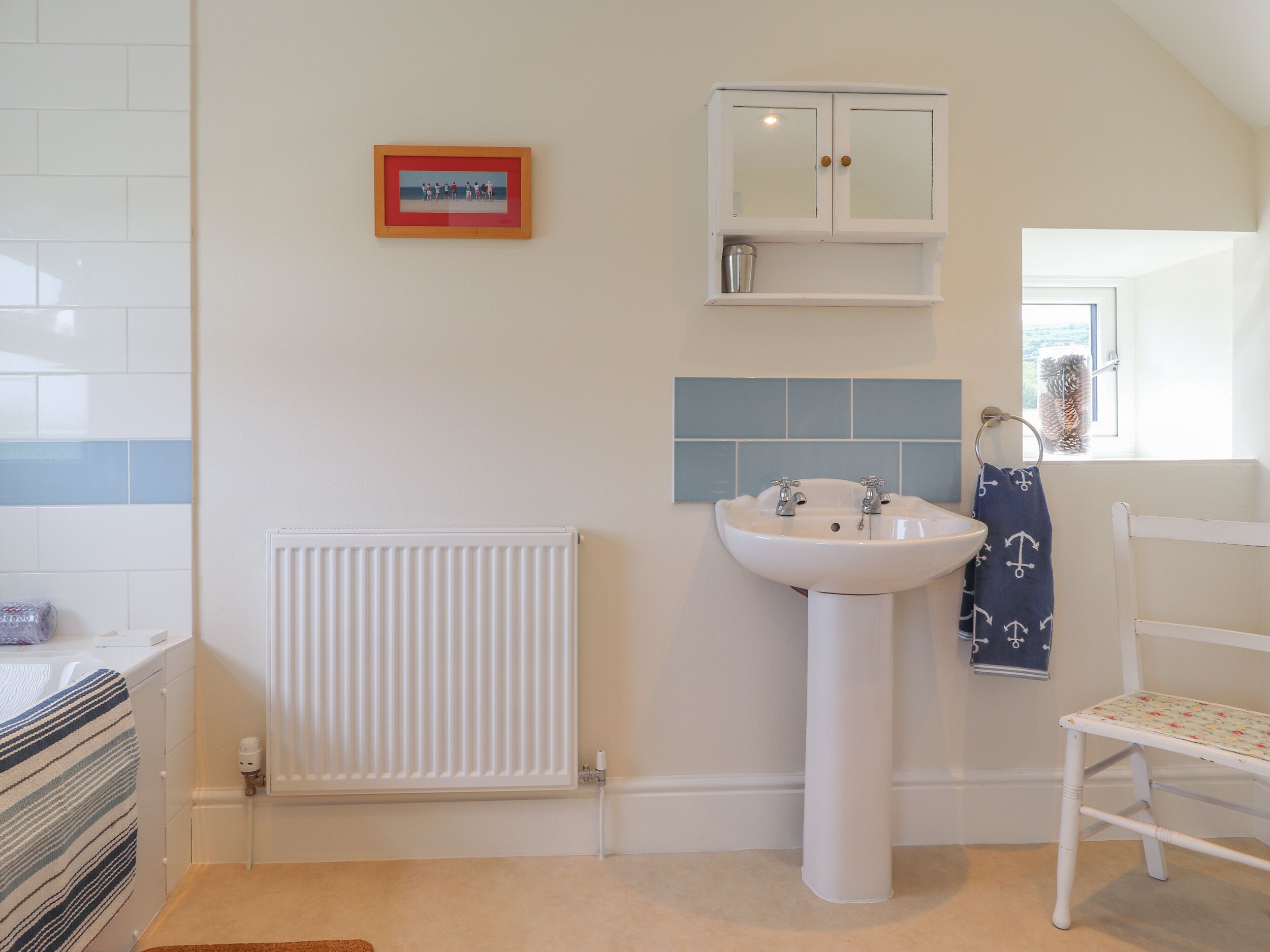 Une salle de bain avec un radiateur blanc, un lavabo blanc, un tableau encadré au mur et un porte-serviettes avec une serviette.
