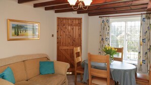 Un salon chaleureux avec un canapé beige, des chaises en bois, une petite table ronde et une porte en bois.