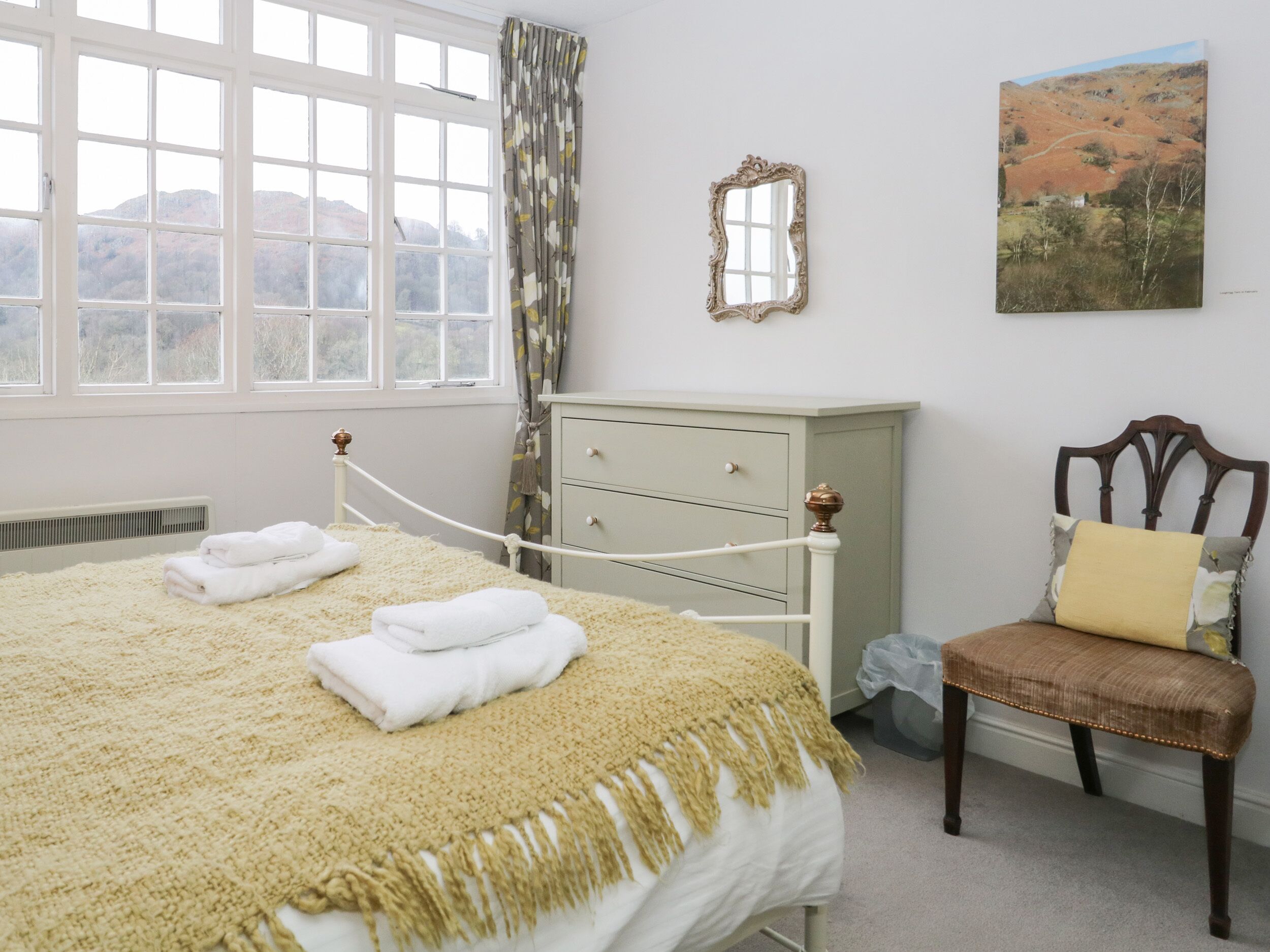 Un dormitorio con cama, una silla, cómoda, espejo y un cuadro en la pared.