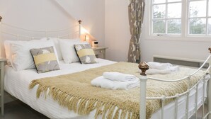 Una cama bien hecha con una colcha blanca y beige, dos almohadas y una mesita de noche con una lámpara.