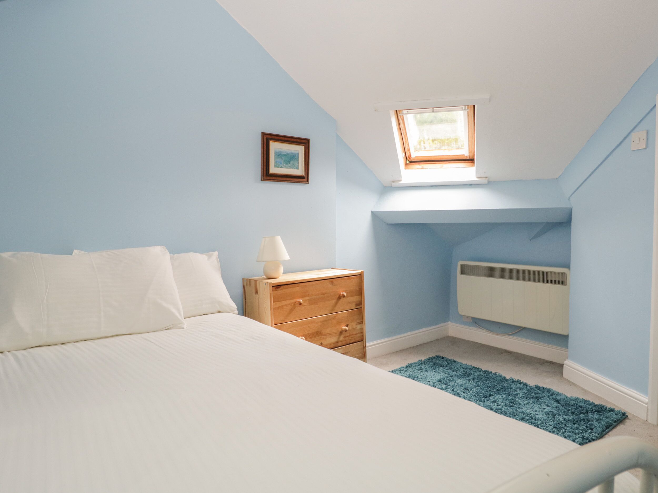 Un dormitorio con cama, mesita de noche, cómoda, ventana y radiador.