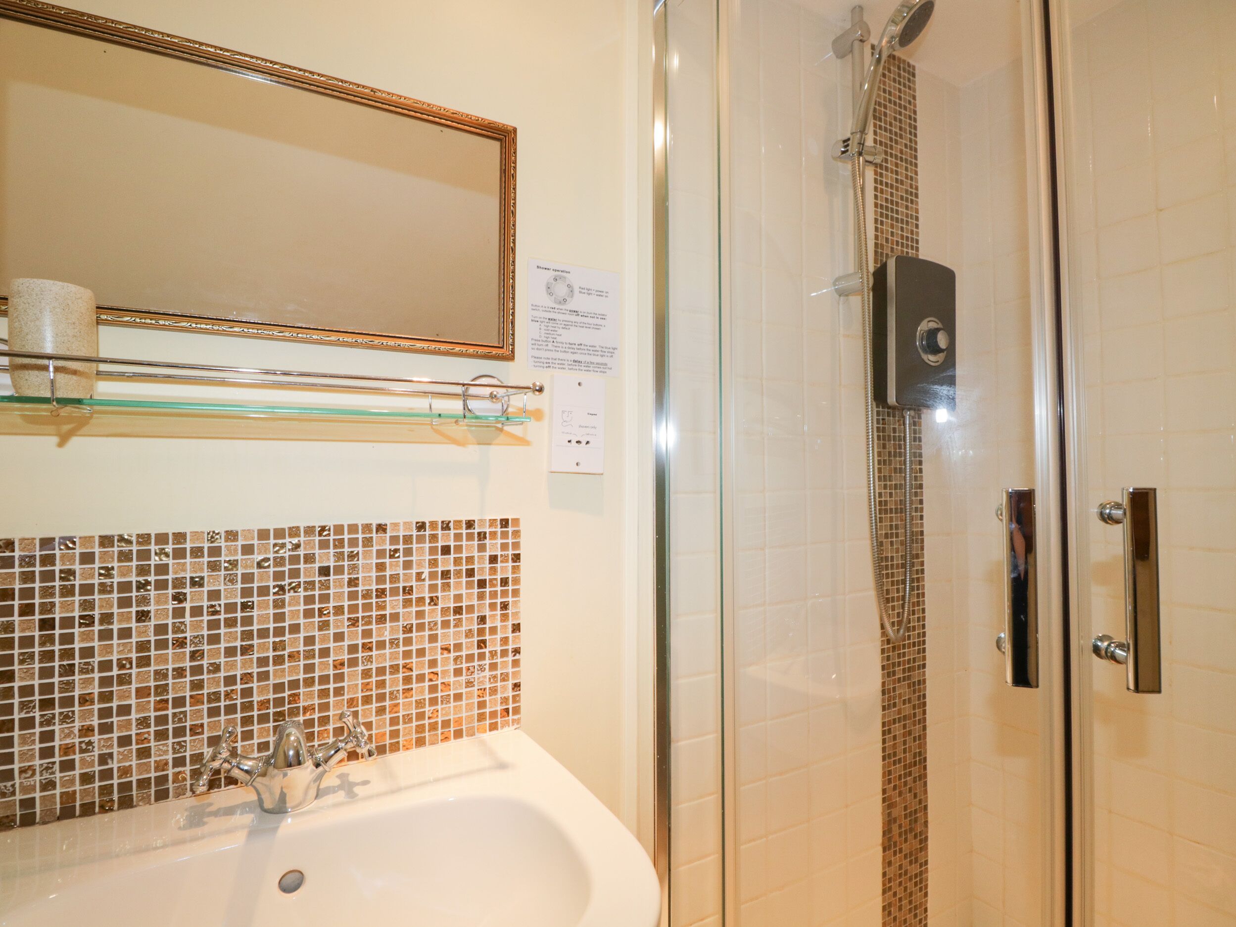 Un bagno con cabina doccia in vetro, un lavabo con specchio sopra e una parete di mosaico.