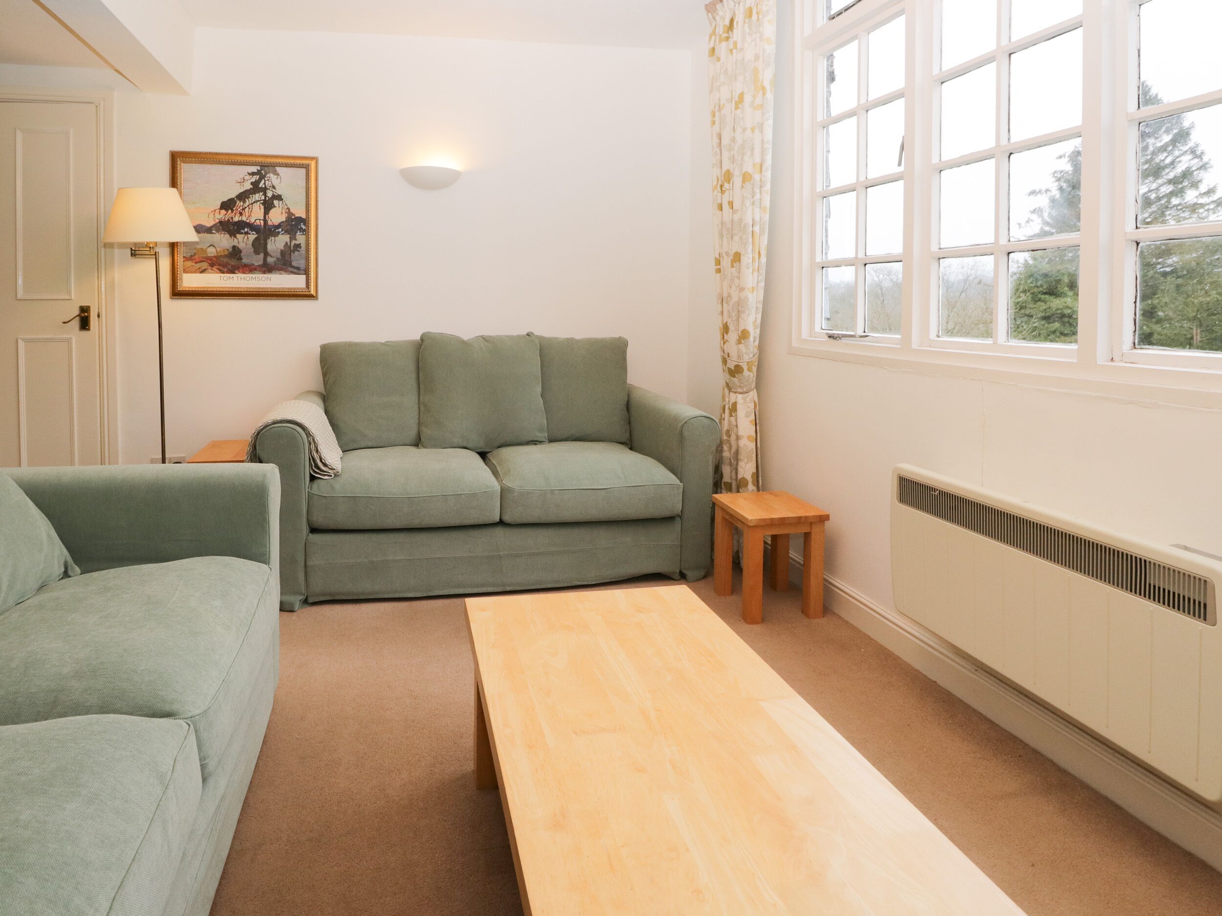 A living room with a sofa, a small wooden table, a lamp, and a window with curtains.
