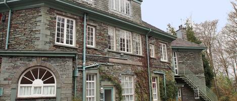 A stone building with a green roof, multiple windows, a front door, and a staircase leading to an upper level.