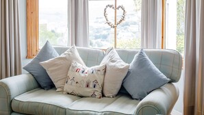 A light blue sofa with a heart-shaped decoration on a window sill, surrounded by various pillows. - Wisteria (St Austell)
