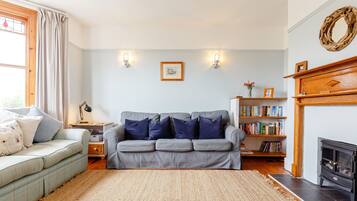 A living room with a grey sofa, a small side table, a bookshelf, and a fireplace.