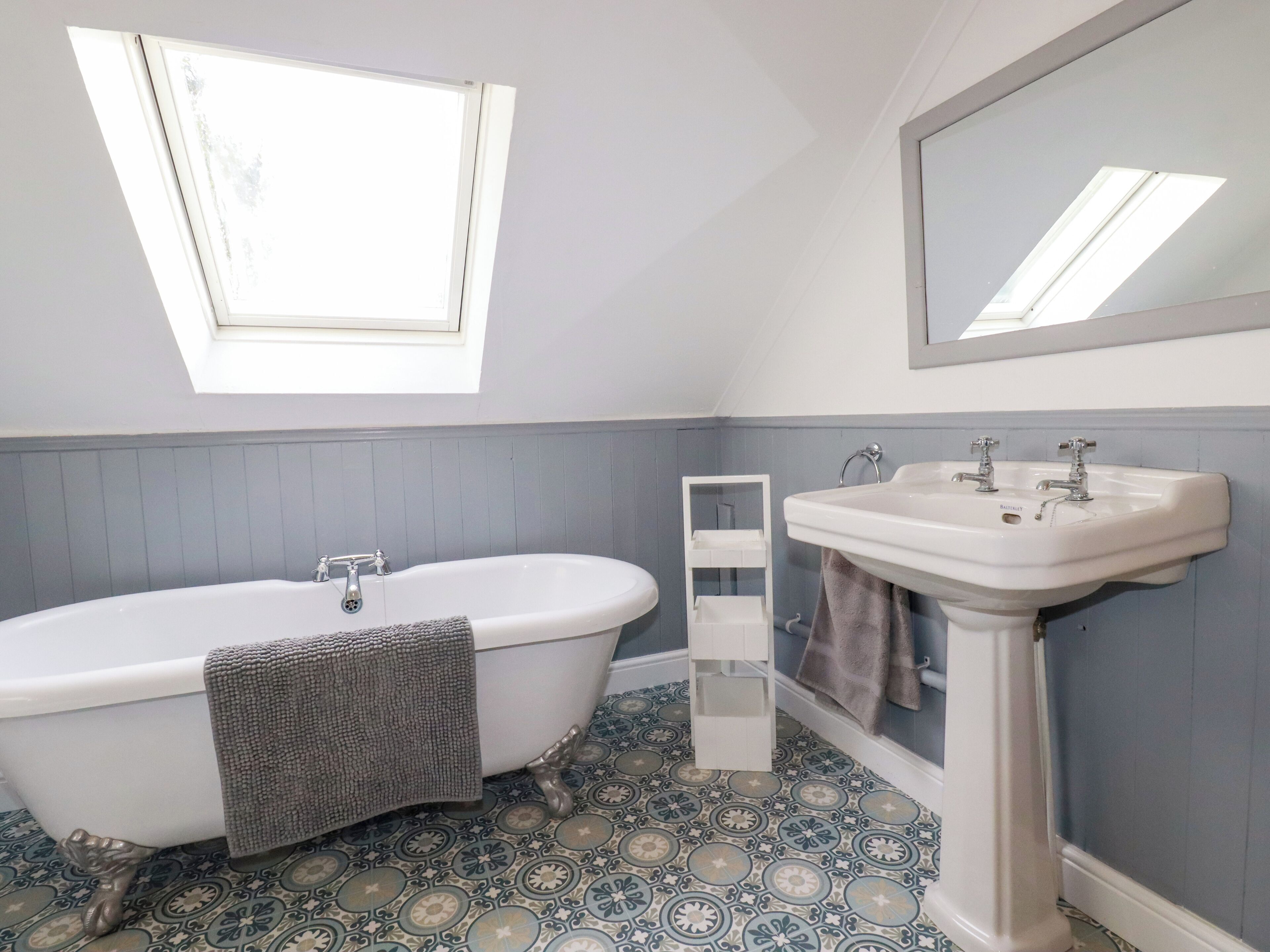A bathroom with a freestanding bathtub, a pedestal sink, and a window above the tub.