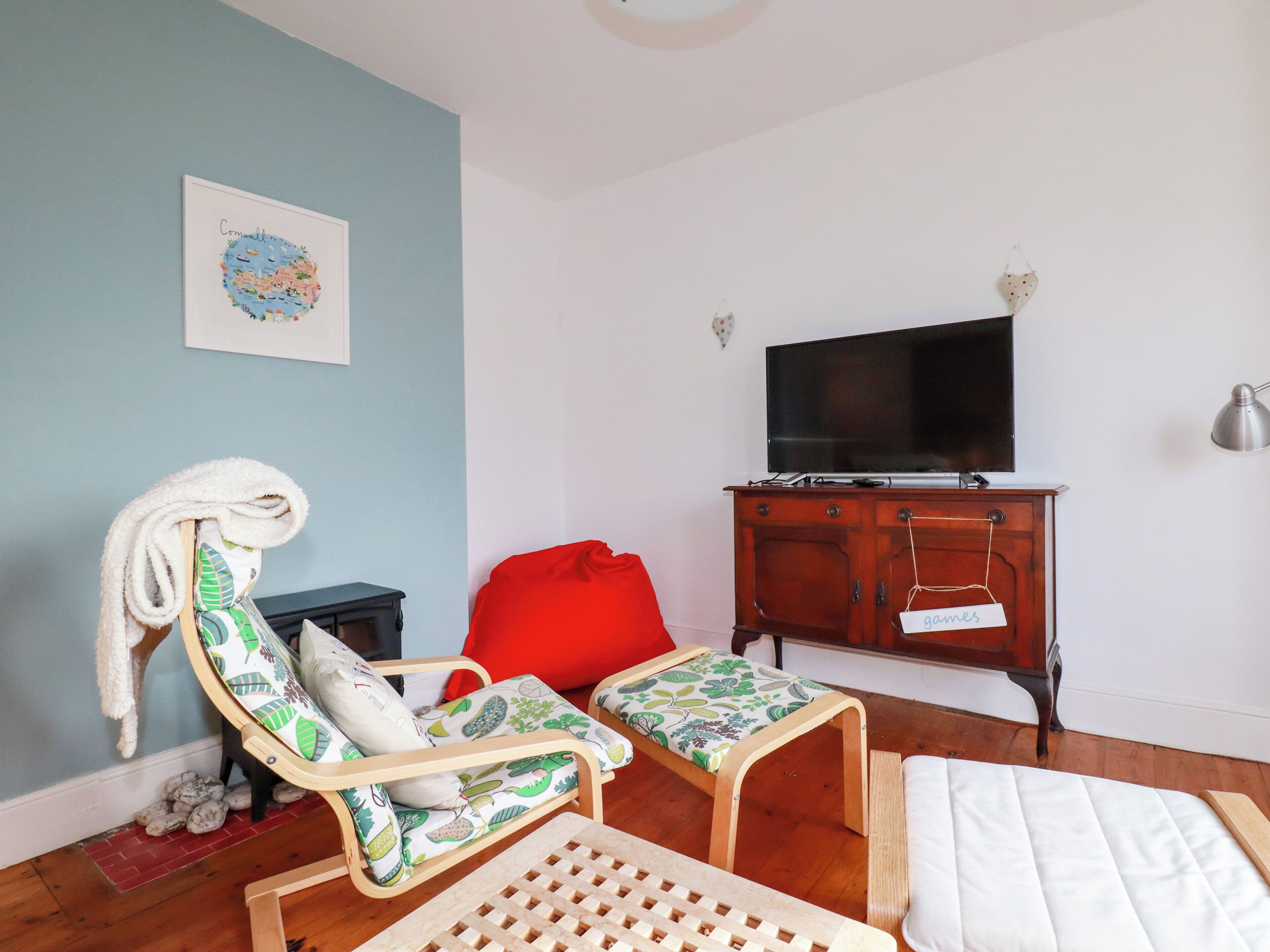 Une pièce avec un plancher en bois, un téléviseur posé sur un meuble en bois, une chaise rouge, une petite table et un lit avec un matelas blanc.