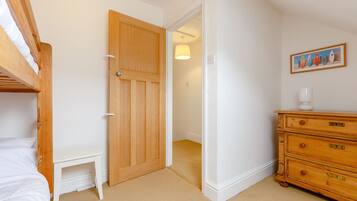 A bedroom with a bunk bed, a wooden dresser, a small bedside table, and a door leading to another room.