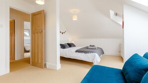 A bedroom with a bed, a blue sofa, and a white ceiling. - Wisteria (St Austell)