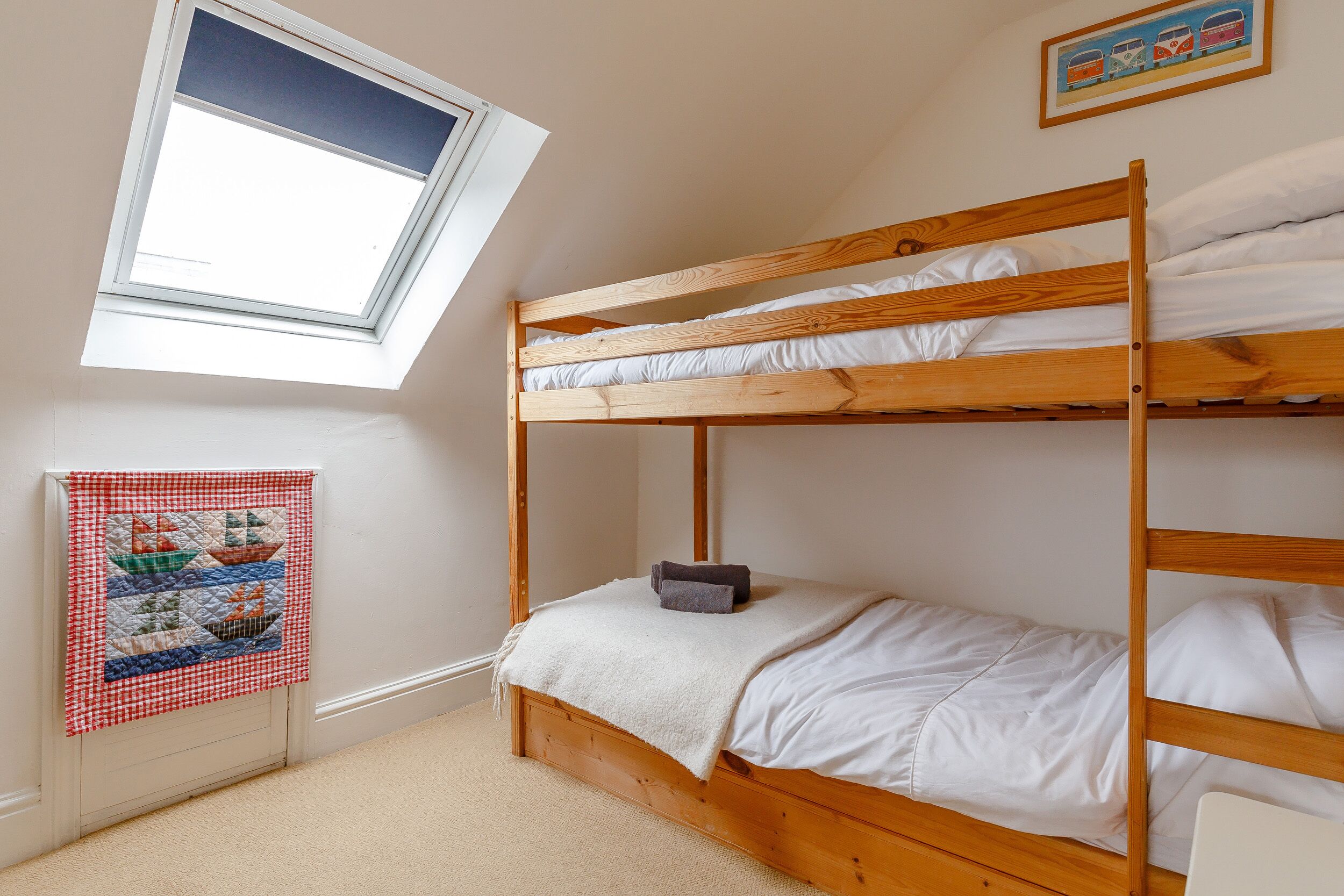 A bunk bed room with a skylight, a quilted wall hanging, and a framed picture.
