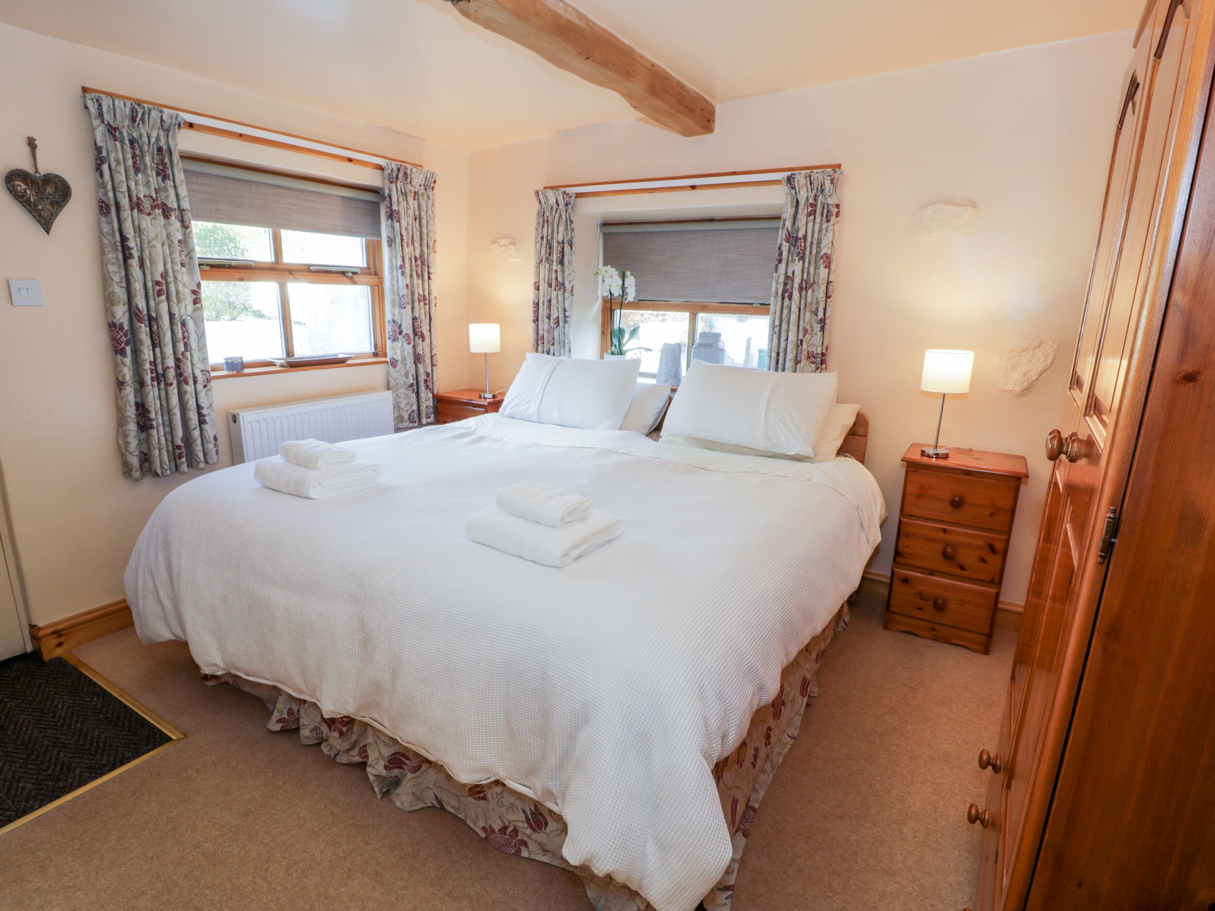 A neatly made bed with white linens and towels, a wooden nightstand with a lamp, and a wooden wardrobe.