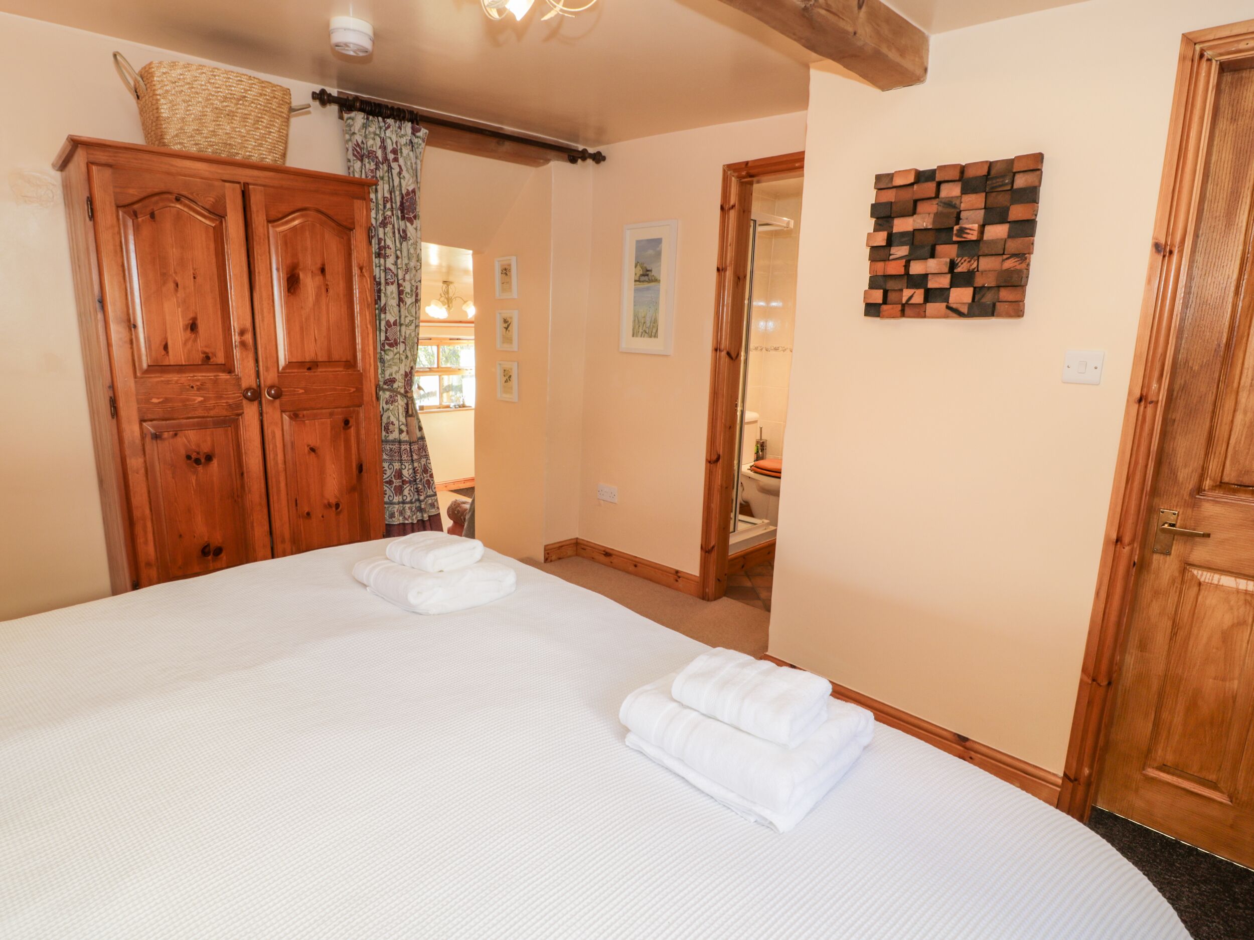 A bedroom with a large bed, wooden wardrobe, and a bathroom visible through an open door.