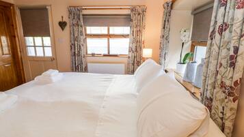 A large bed with white linens, a wooden door, and a window with floral curtains.