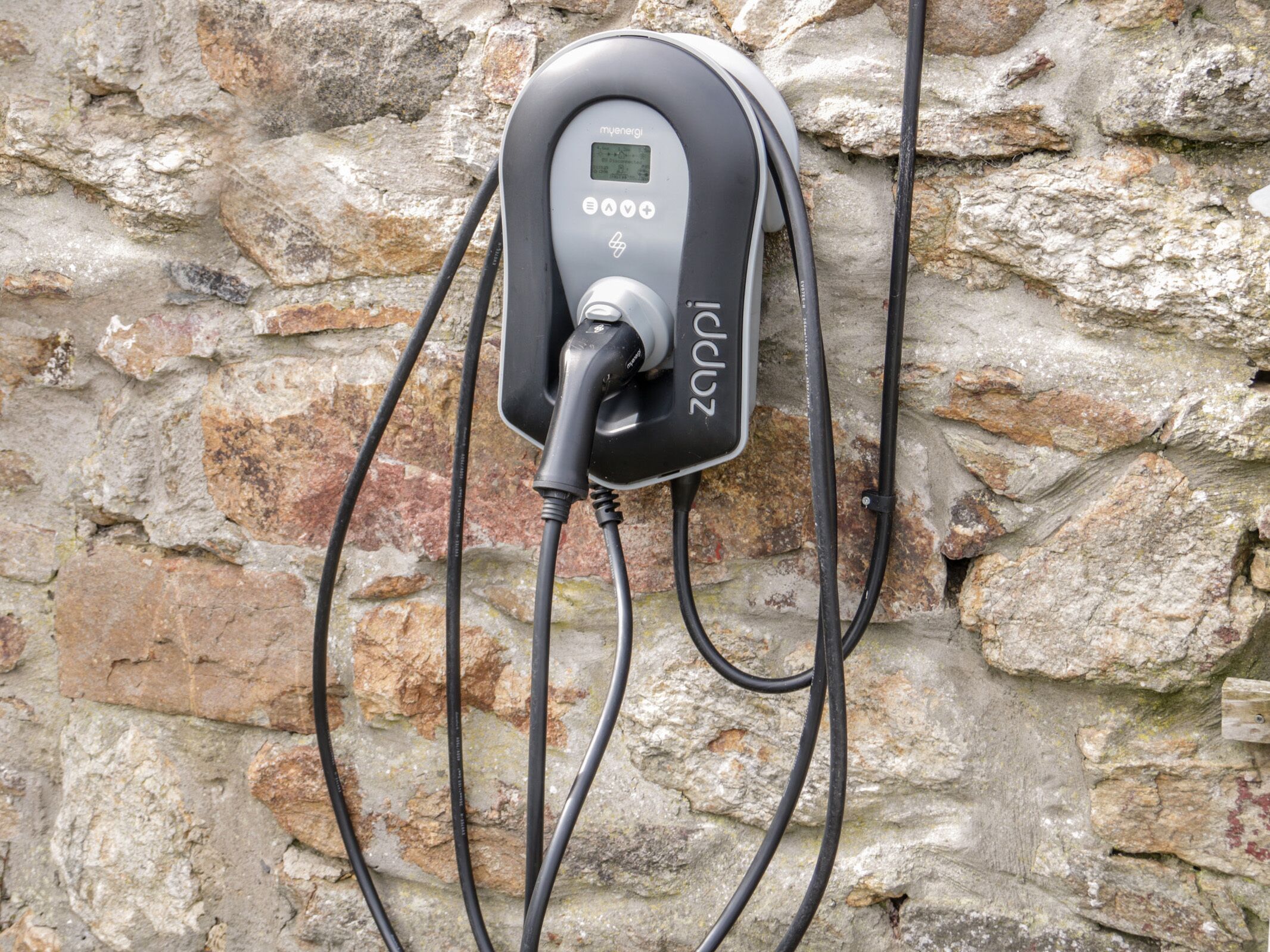 An electric vehicle charging station mounted on a stone wall.
